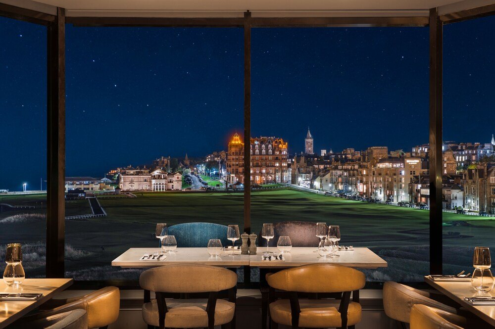 Mesa para dos junto a ventanales con vista nocturna al campo de golf