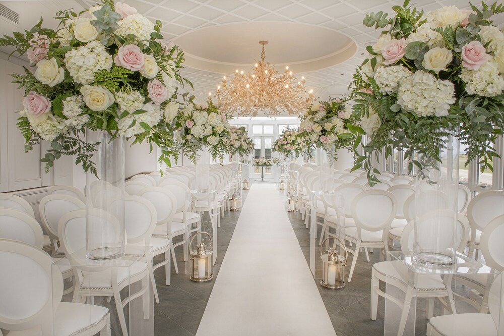 Pasillo de boda con sillas blancas y arreglos florales